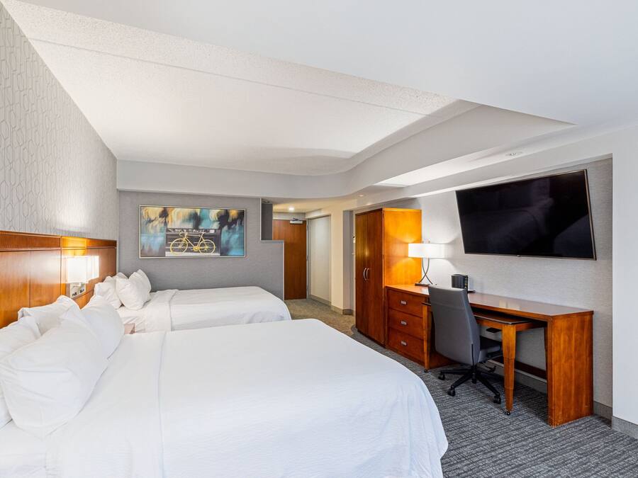 Habitación de hotel con dos camas, un escritorio, un televisor y un cuadro en la pared.