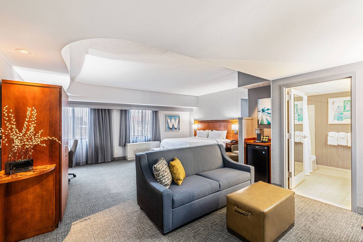 A hotel room with a bed, a sofa, a desk, and a bathroom.