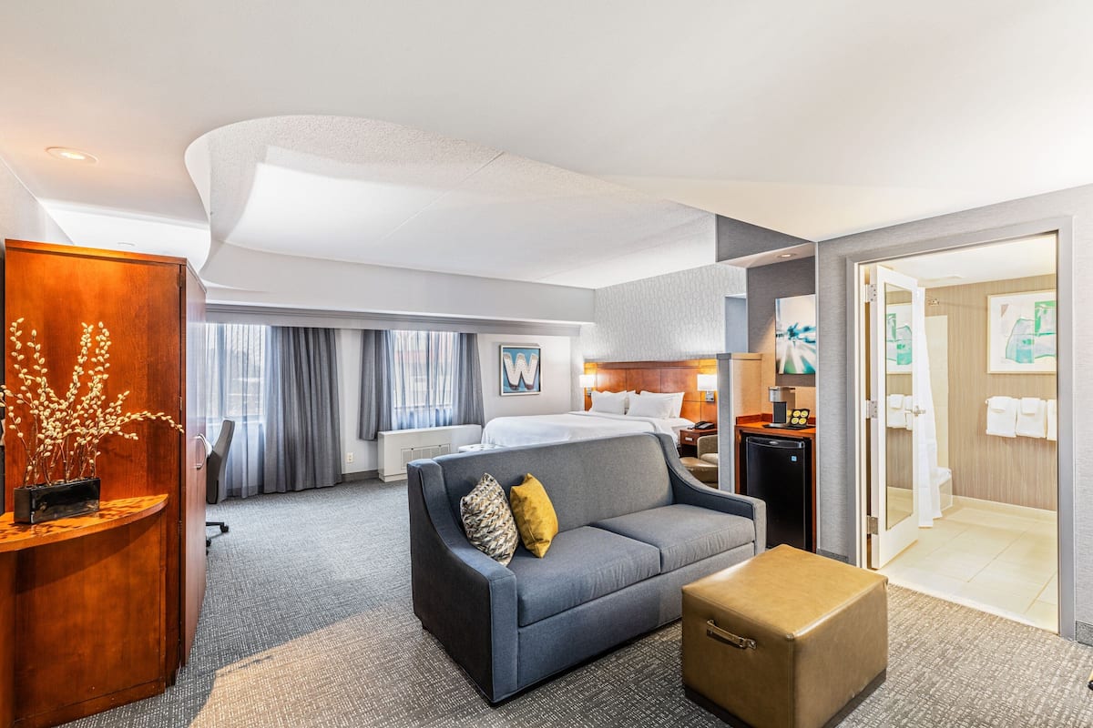 A hotel room with a bed, a sofa, a desk, and a bathroom.