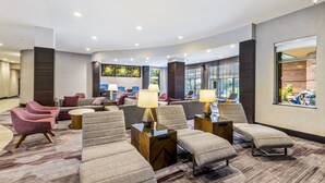 A modern hotel lobby with seating areas, a reception desk, and a large window with a view of the outdoors. - Courtyard by Marriott Boston Waltham (Waltham)