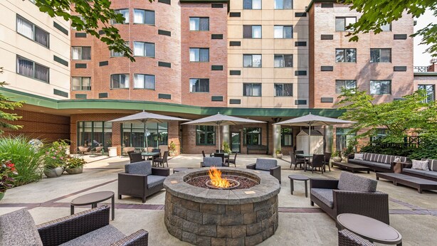 A courtyard with a fire pit, outdoor seating, and a brick building in the background. - Courtyard by Marriott Boston Waltham (Waltham)