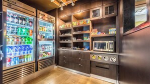 Una piccola cucina attrezzata con frigorifero, forno a microonde ed scaffali pieni di snack e bevande.
