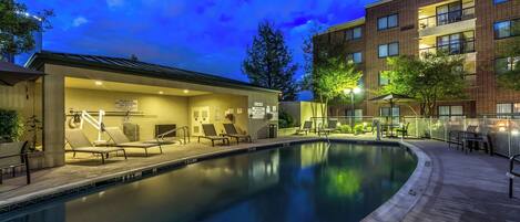 A swimming pool with lounge chairs and a covered area, surrounded by a brick building with multiple balconies.