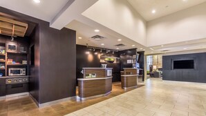 Una moderna hall d'hotel con una reception, un'area salotto e una cucina con elettrodomestici.