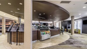 Una moderna hall d'albergo con una reception a forma di semicircolo, un angolo caffè self-service e una zona salotto con divano e poltrone.
