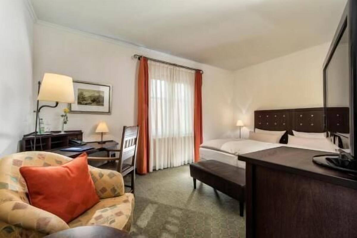 A hotel room with a bed, a desk, a chair, a sofa, and a television.