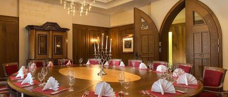 Un comedor formal con una gran mesa ovalada, sillas tapizadas en rojo y un candelabro.