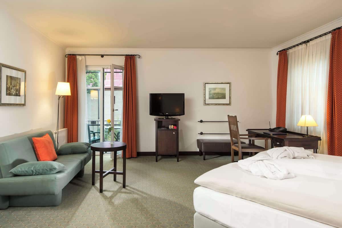 A hotel room with a bed, a sofa, a desk with a chair, a TV, and a small table.