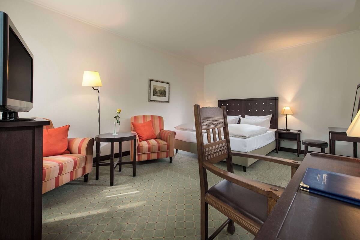 A hotel room with a bed, a sofa, a chair, a desk, a television, and a lamp.