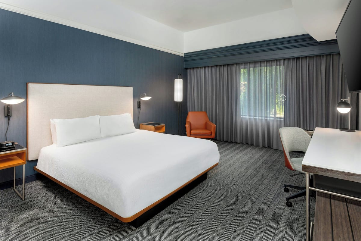 A hotel room with a large bed, a desk, a chair, and a TV.