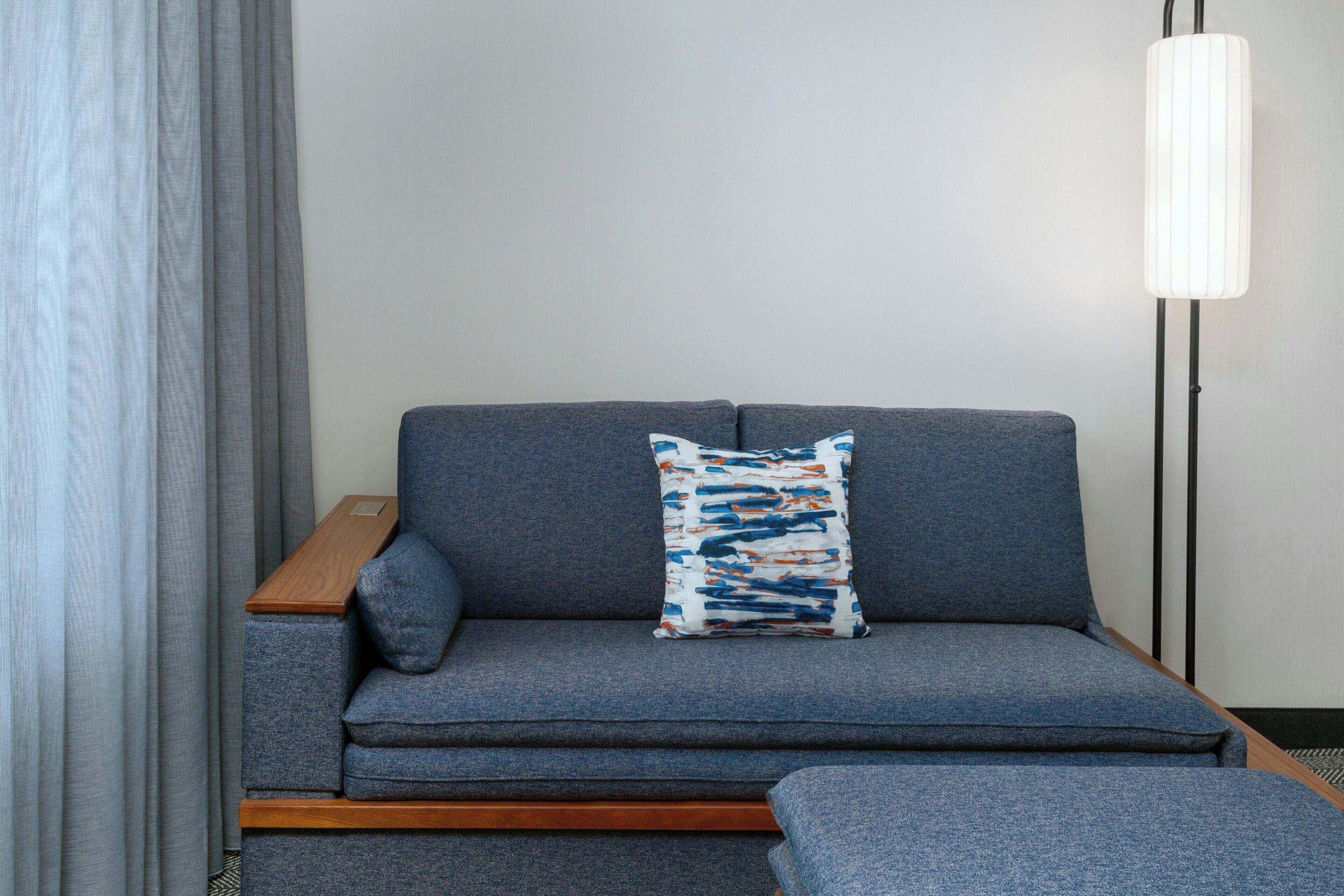 En modern soffa med en mönstrad kudde, ett träbord och en golvlampa.