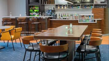 A modern bar area with a long counter, multiple stools, and a variety of bottles and glasses.
