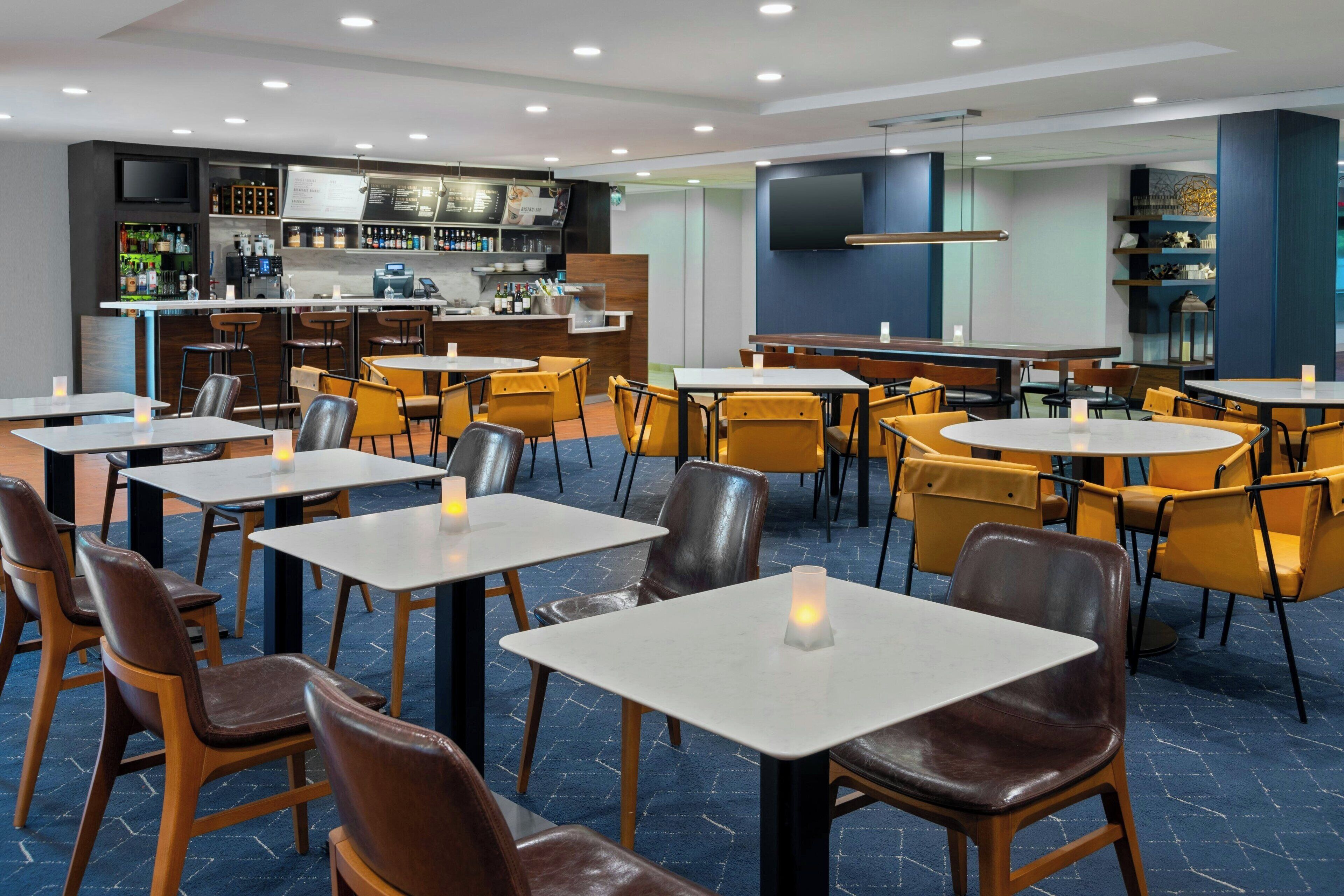 Um restaurante moderno com várias mesas, cadeiras, um bar e uma tela de televisão.