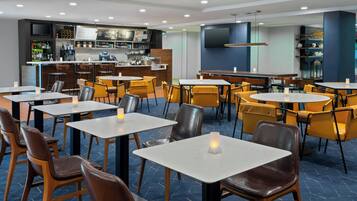 Um restaurante moderno com várias mesas, cadeiras, um bar e uma tela de televisão.