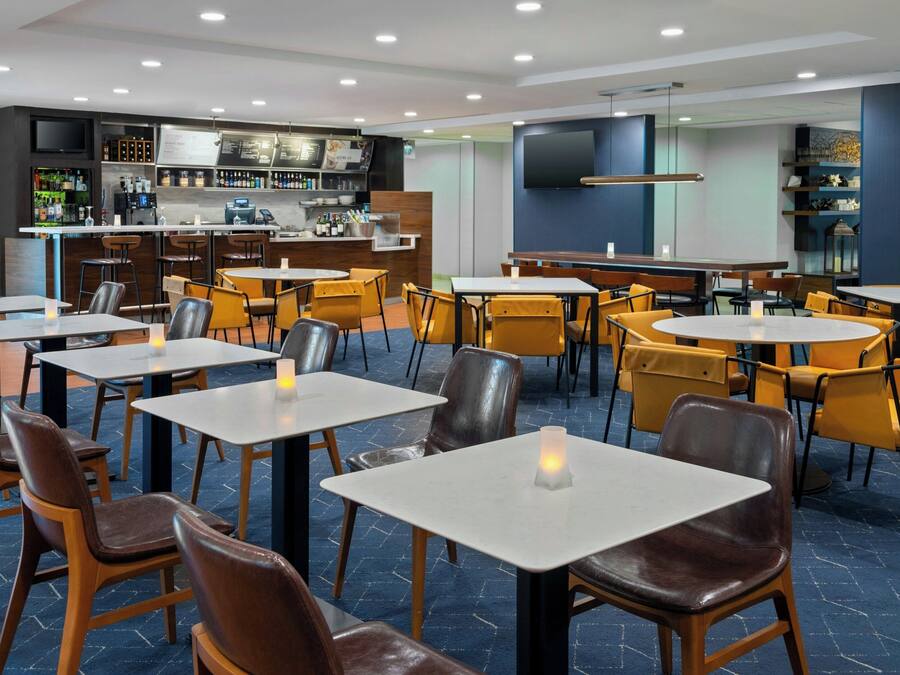Um restaurante moderno com várias mesas, cadeiras, um bar e uma tela de televisão.