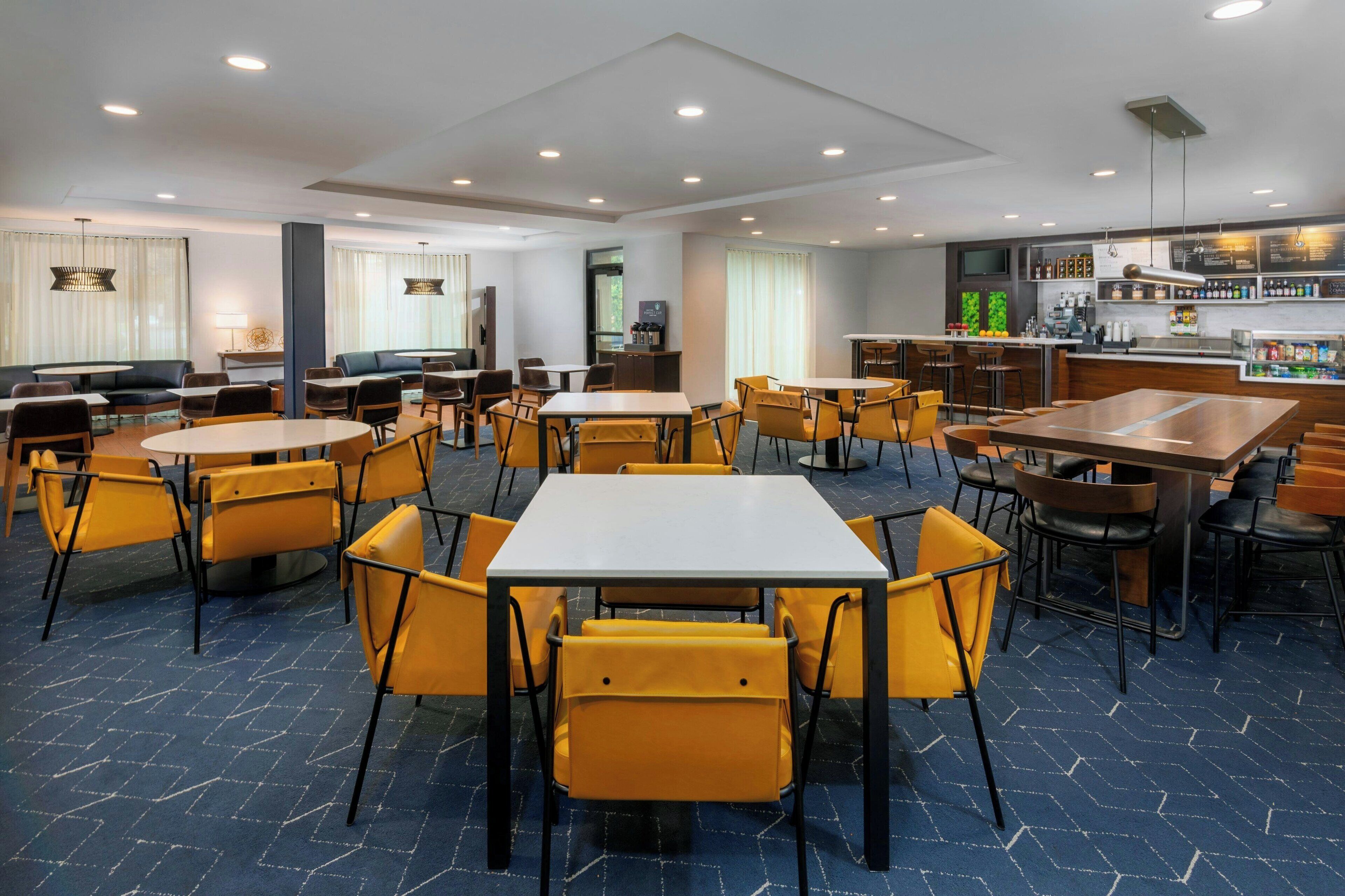A hotel dining area with multiple tables and chairs, a bar, and a television.