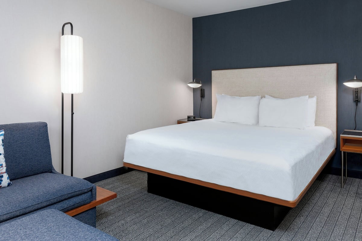 A hotel room with a large bed, a sofa, a standing lamp, and a nightstand.