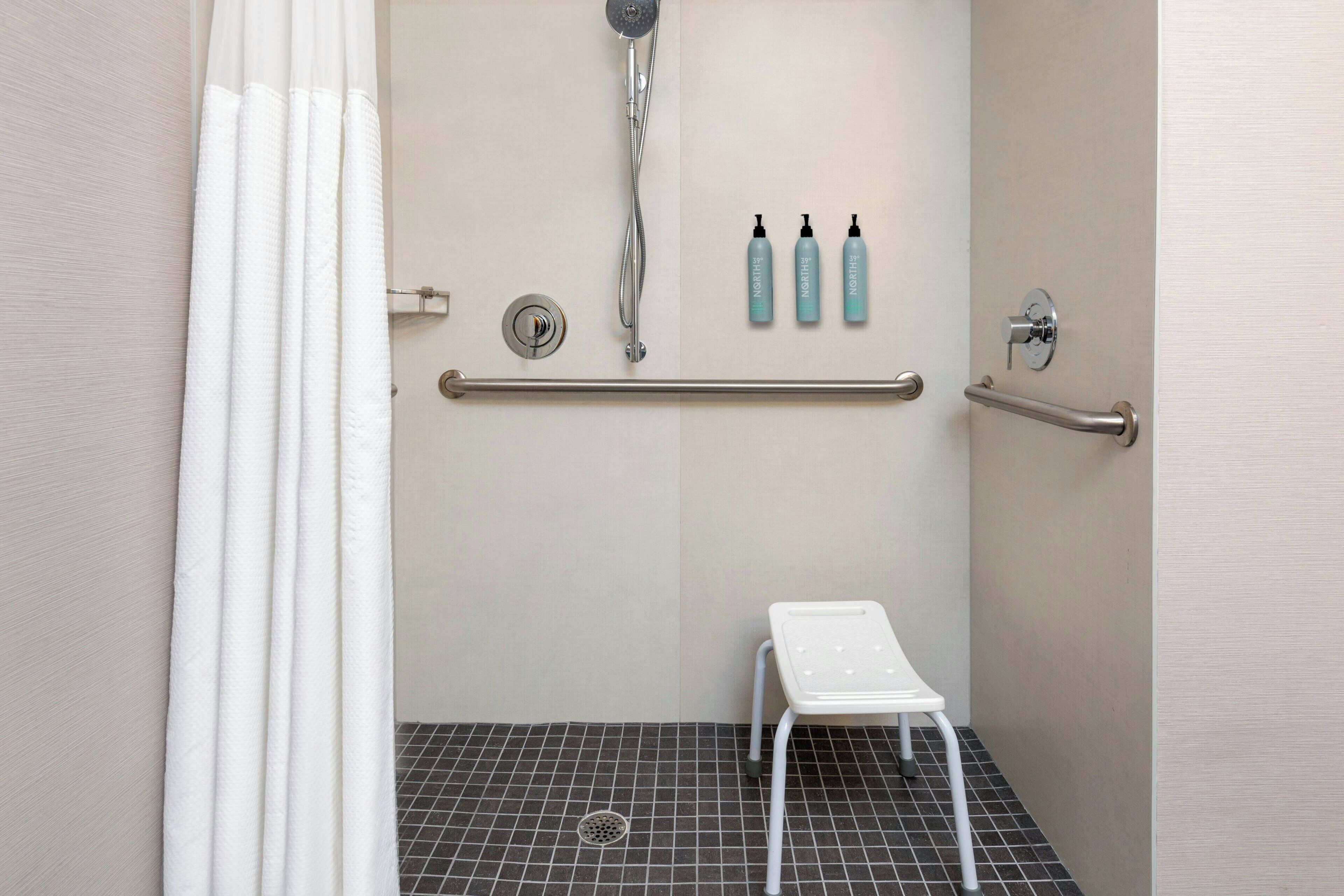 Eine Dusche mit Handbrause, einer weißen Sitzbank und zwei Flaschen Shampoo und Conditioner an der Wand.
