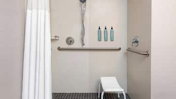 Eine Dusche mit Handbrause, einer weißen Sitzbank und zwei Flaschen Shampoo und Conditioner an der Wand.