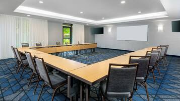 A conference room with a long table, chairs, a projector screen, and a large window with curtains.