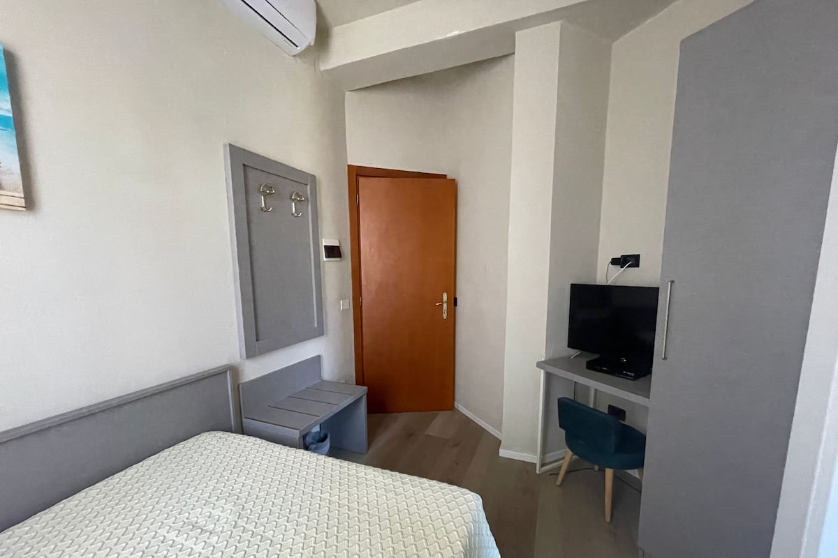 A hotel room with a bed, a desk with a television, a wardrobe, and a door.