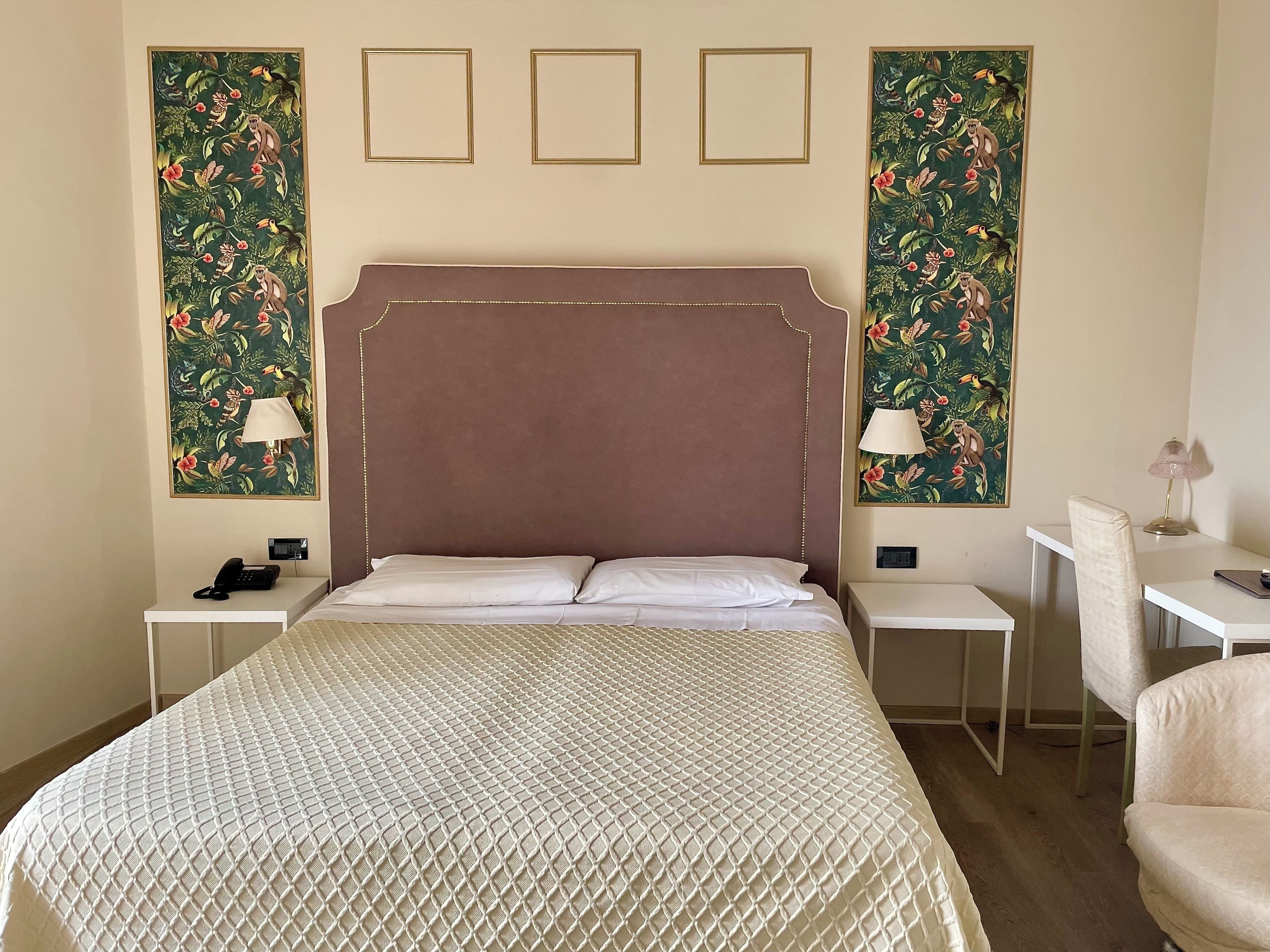 Een hotelkamer met een groot bed, twee nachtkastjes, een bureau en een stoel. Er hangen drie ingekaderde foto's aan de muur.