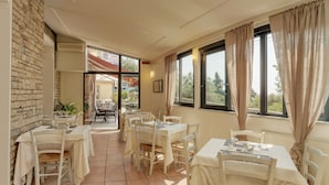 A restaurant with outdoor seating, stone walls, and large windows with curtains. - Hotel Rosa dei Venti (Lerici)
