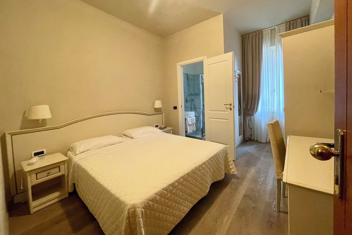 A hotel room with a bed, bedside tables, a desk, and a bathroom visible through an open door.