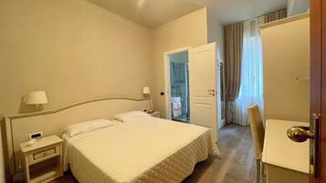 Habitación de hotel con cama, mesitas de noche, un escritorio y un baño visible a través de una puerta abierta.