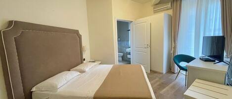 Habitación de hotel con cama, escritorio, silla, televisión y aire acondicionado.
