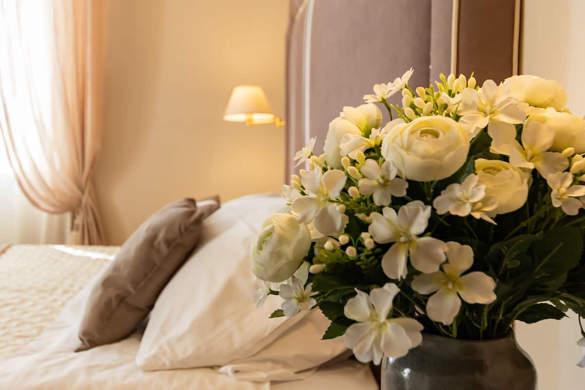 A hotel room with a bed, a nightstand, a lamp, and a vase with flowers.
