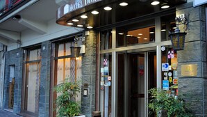 L’entrée d’un hôtel, avec une façade en pierre, de grandes portes vitrées et de nombreux luminaires.