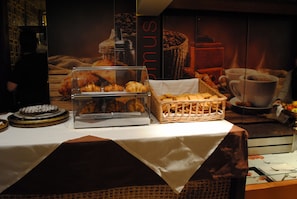 Un buffet de petit-déjeuner comprenant des viennoiseries, une machine à café et un panier de pain.