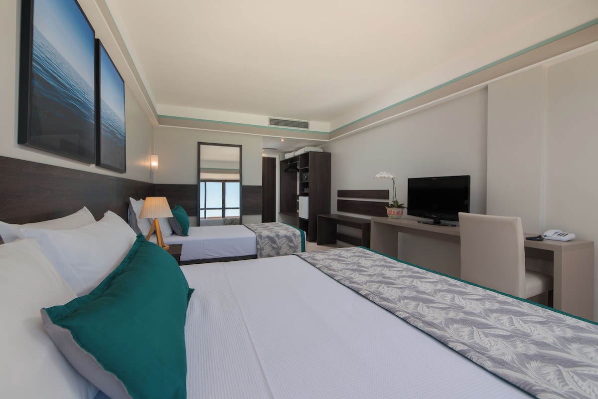 Een hotelkamer met twee bedden, een bureau, een televisie en een badkamer die door een open deur zichtbaar is.