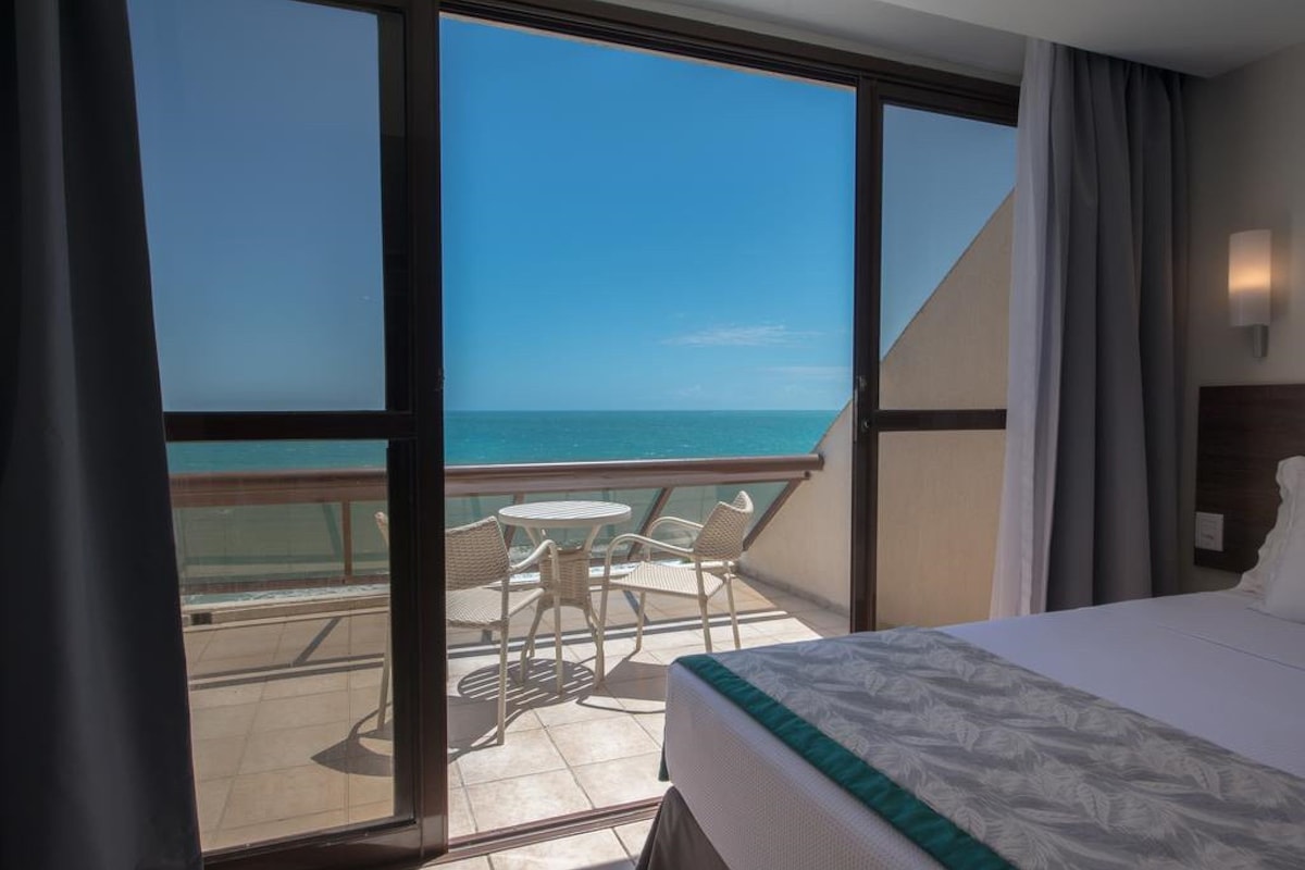 Een hotelkamer met balkon, een bed en uitzicht op de oceaan.