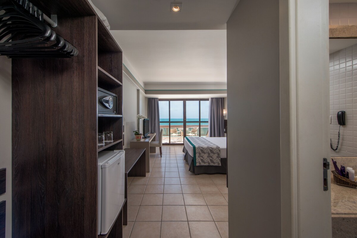 A hotel room with a balcony, a bed, a desk, and a wardrobe.