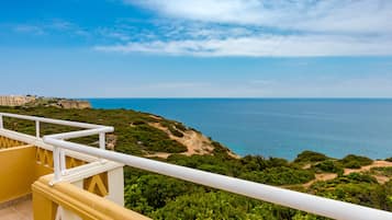 A balcony with a white railing overlooking a coastal landscape with buildings in the distance.