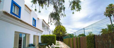 Un patio con una fila de tumbonas blancas, una mesita y una zona de césped verde.