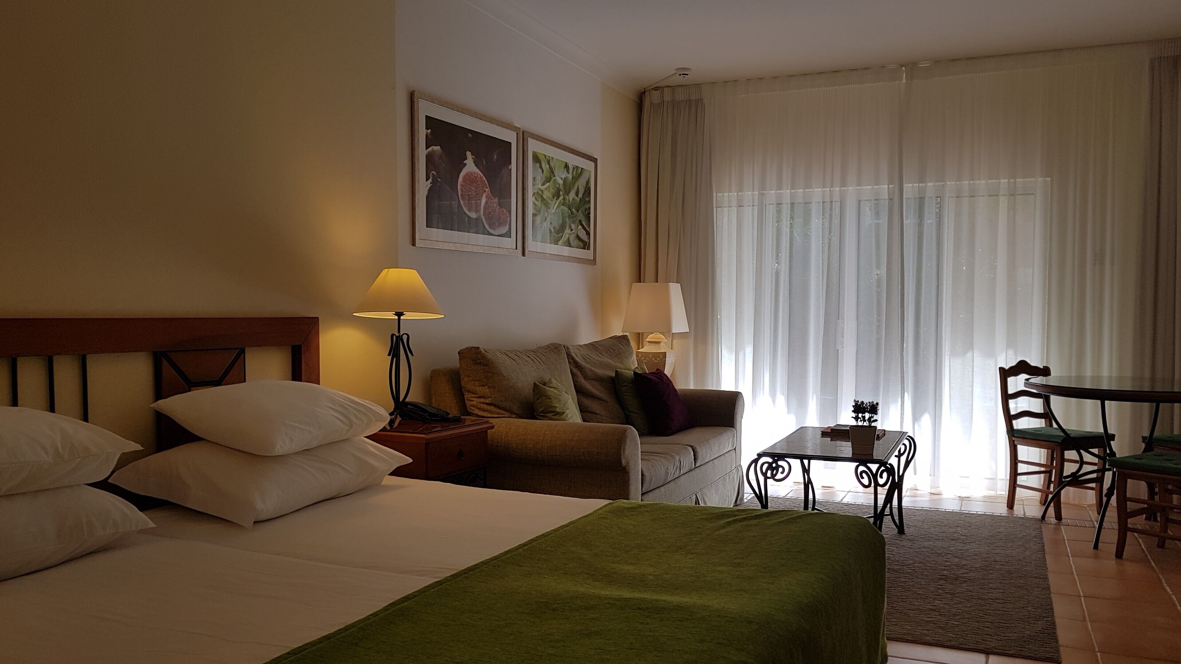 Habitación de hotel con cama, sofá, una mesita y una silla. Hay dos lámparas en las mesitas de noche.