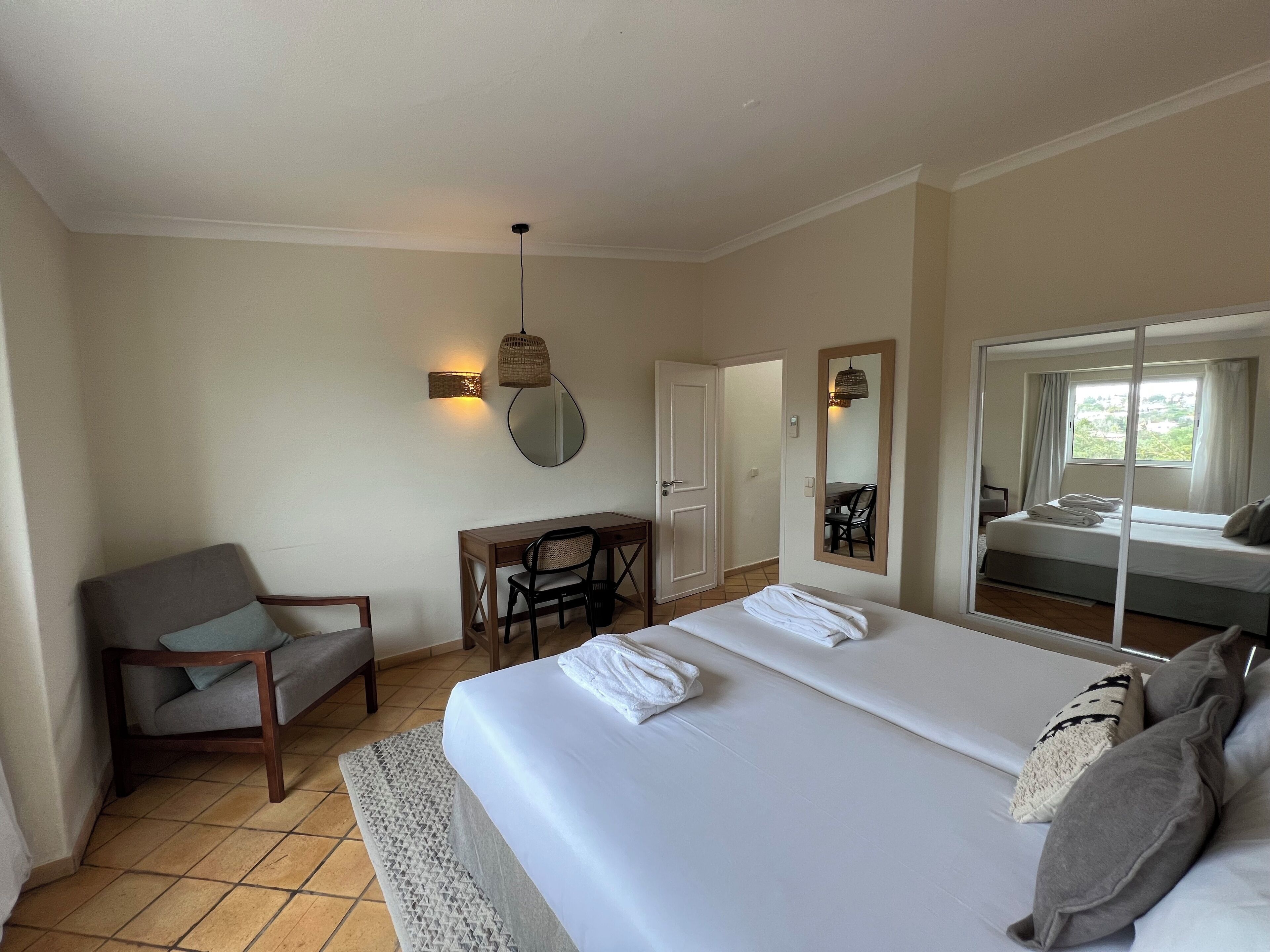 A hotel room with a bed, a desk, a chair, a mirror, and a window.