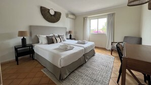 Quarto de hotel com duas camas, uma mesa de jantar e uma janela com cortinas.
