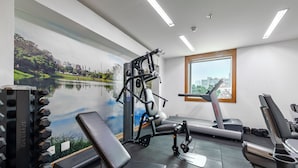 Une salle de sport équipée de matériel d’exercice, d’un tapis de course et d’une grande fenêtre donnant sur la ville.