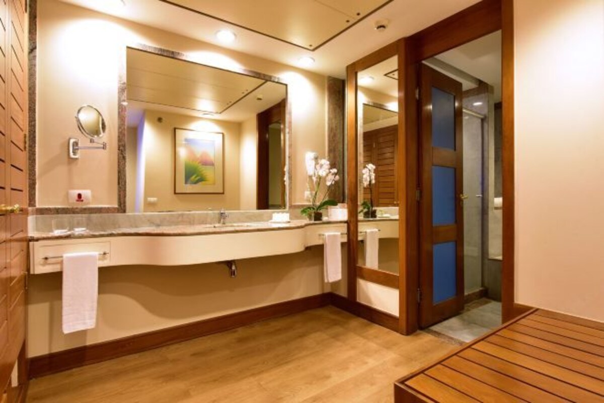 A modern bathroom with a large mirror, wooden flooring, and a wooden bench.