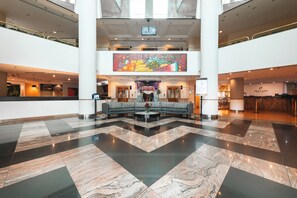 Een ruime lobby met een geruit vloertapijt, een centraal zitgedeelte en een grote muurschildering op het bovenste niveau.