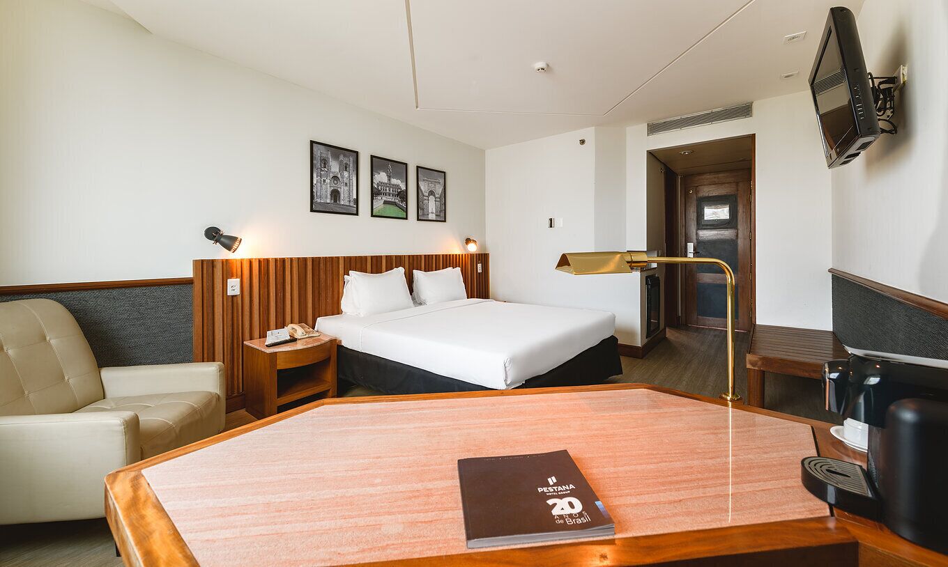 Habitación de hotel con una cama, escritorio, silla, mesita de noche y televisor.