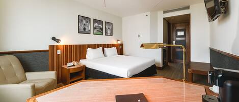 Habitación de hotel con una cama, escritorio, silla, mesita de noche y televisor.