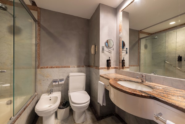A modern bathroom with a glass shower enclosure, a bidet, a toilet, and a marble countertop with a sink.