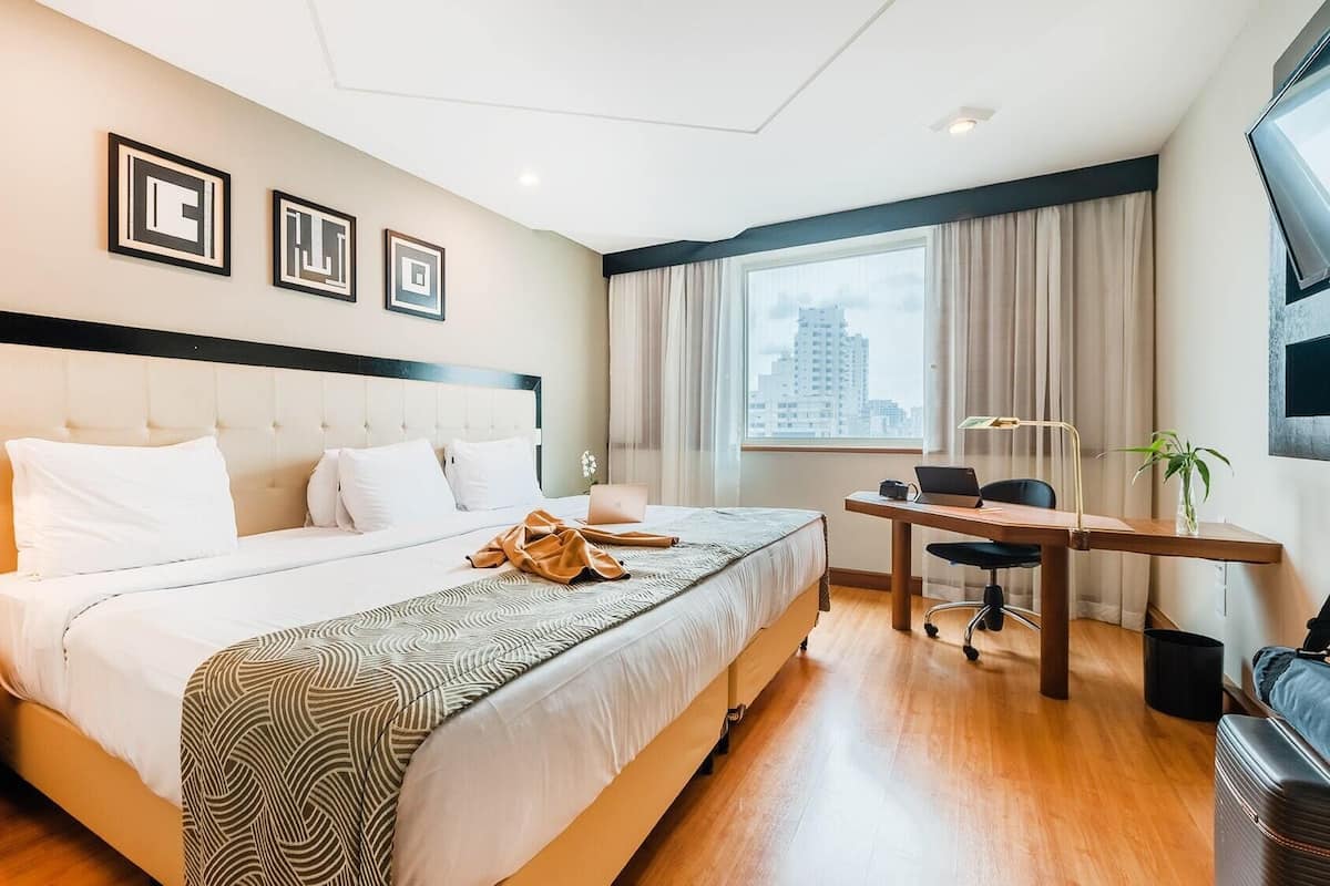 Ein Hotelzimmer mit Bett, Schreibtisch, Stuhl, Lampe und Blick auf die Stadt.