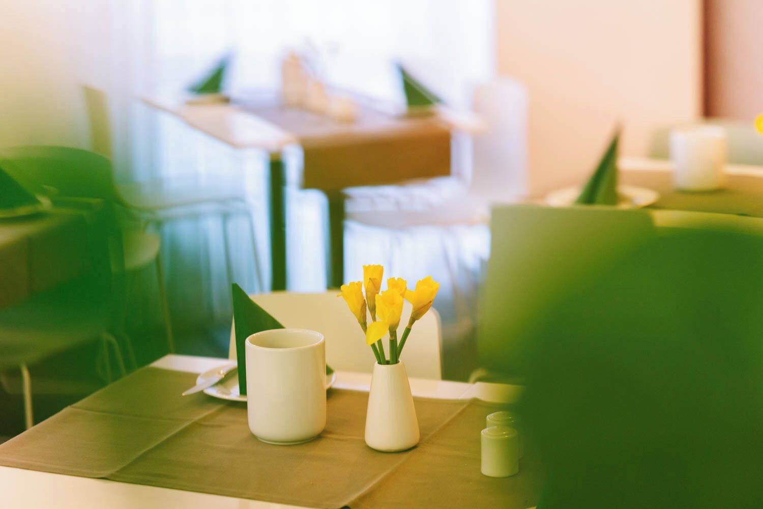 A dining area with a table set for two, featuring a vase with yellow flowers and a white mug.