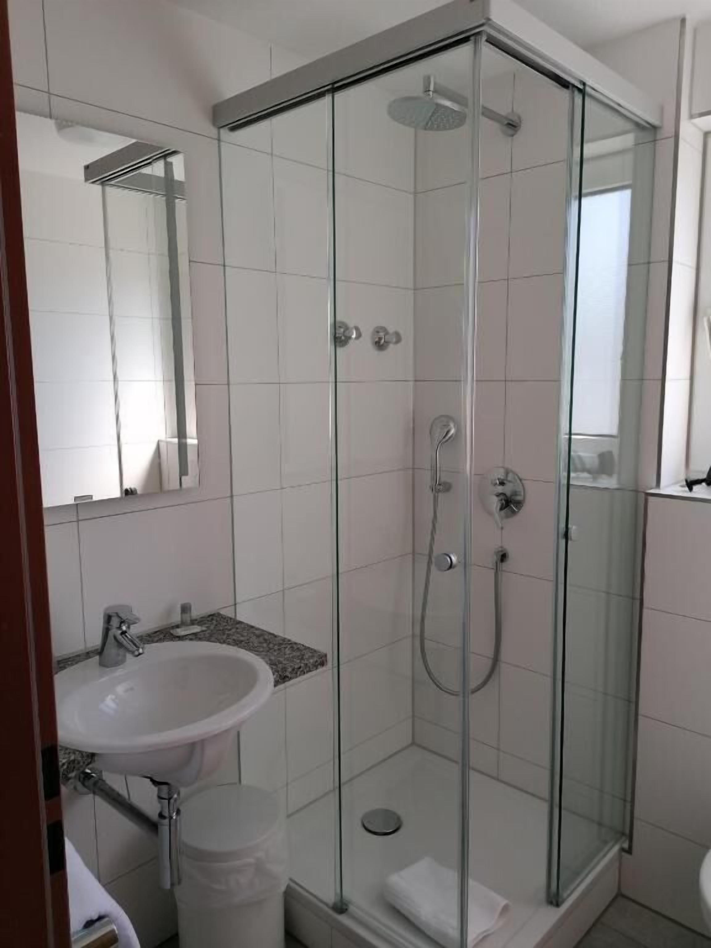 Ein modernes Badezimmer mit einer Duschkabine, einem weißen Waschbecken und einem Spiegel.